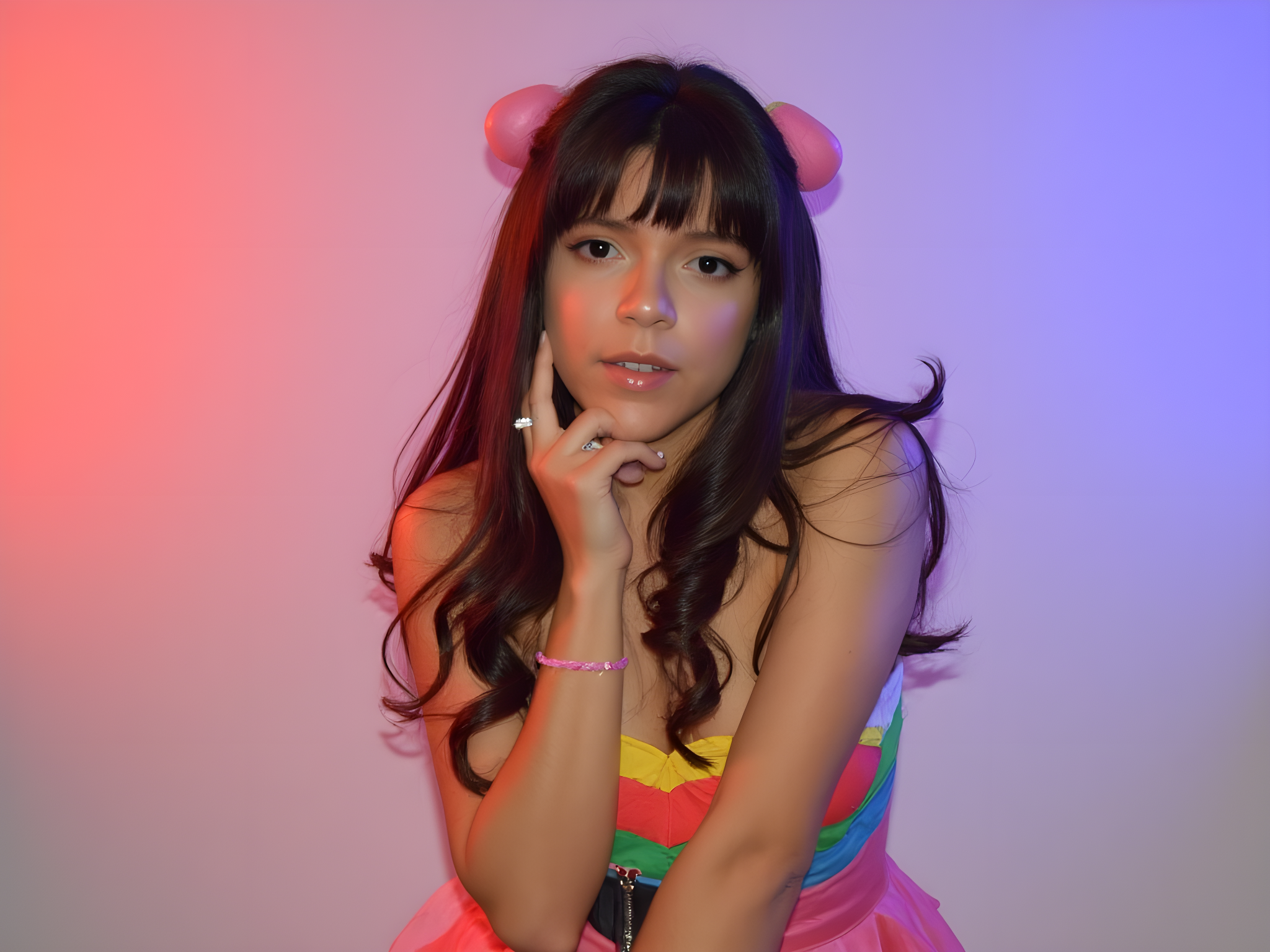 Young woman posing in colorful outfit with heart-shaped pink hair accessories, illuminated by vibrant red and blue lighting for a trendy, modern aesthetic.