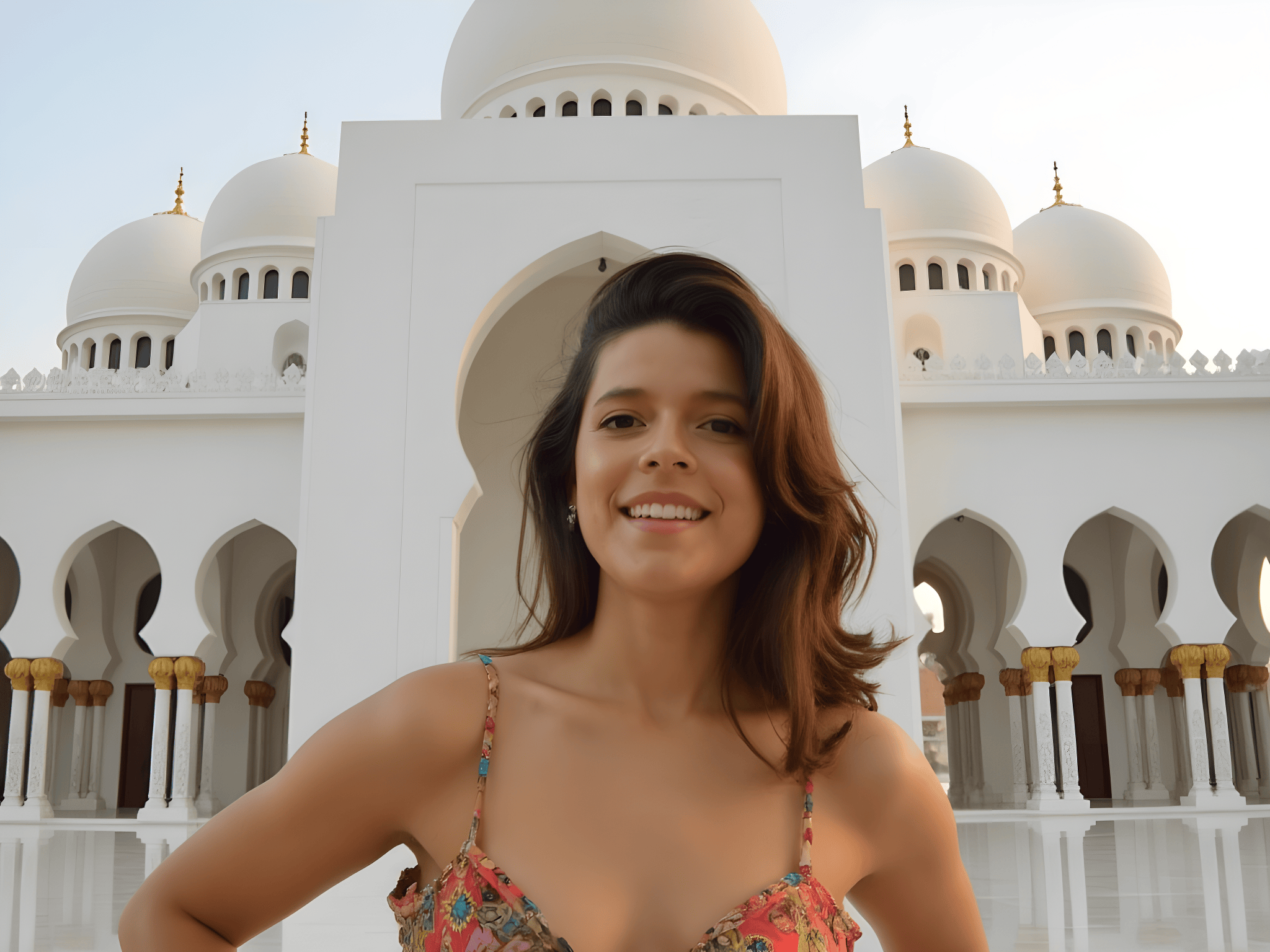 Smiling woman in front of ornate white architecture with domes and arches during sunset.
