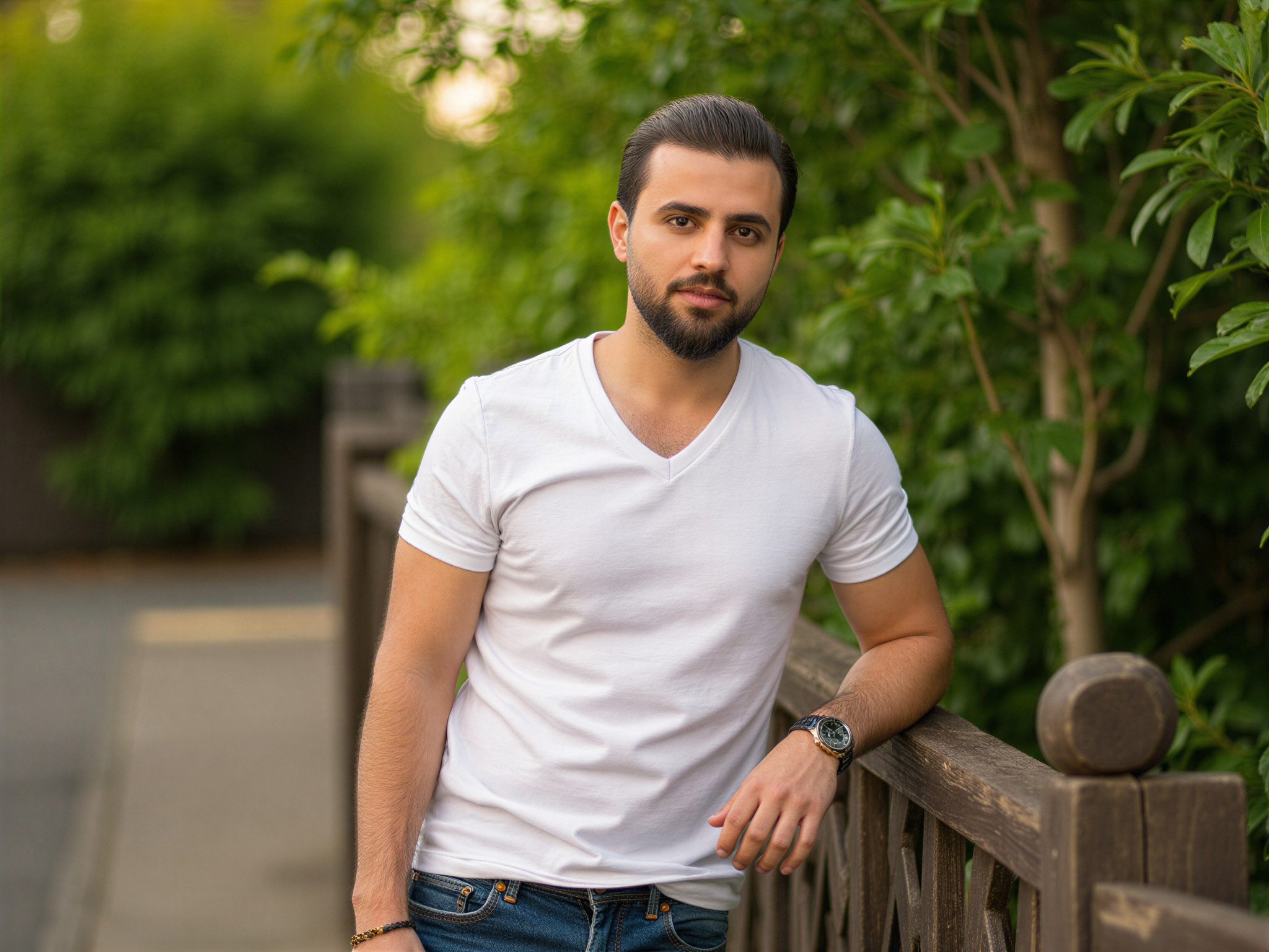 A 32-year-old male, OD62S, exuding warmth and charisma, featured in a candid lifestyle shot that captures the joy of modern dating. He is casually dressed in a soft, fitted white t-shirt paired with stylish denim jeans, standing outdoors with lush greenery in the background. His genuine smile and engaging gaze create an inviting atmosphere, embodying the excitement of making connections on platforms like Ok Cupid. The soft, natural lighting enhances the cheerful mood, emphasizing the happiness in his expression as he leans casually against a vintage wooden fence.