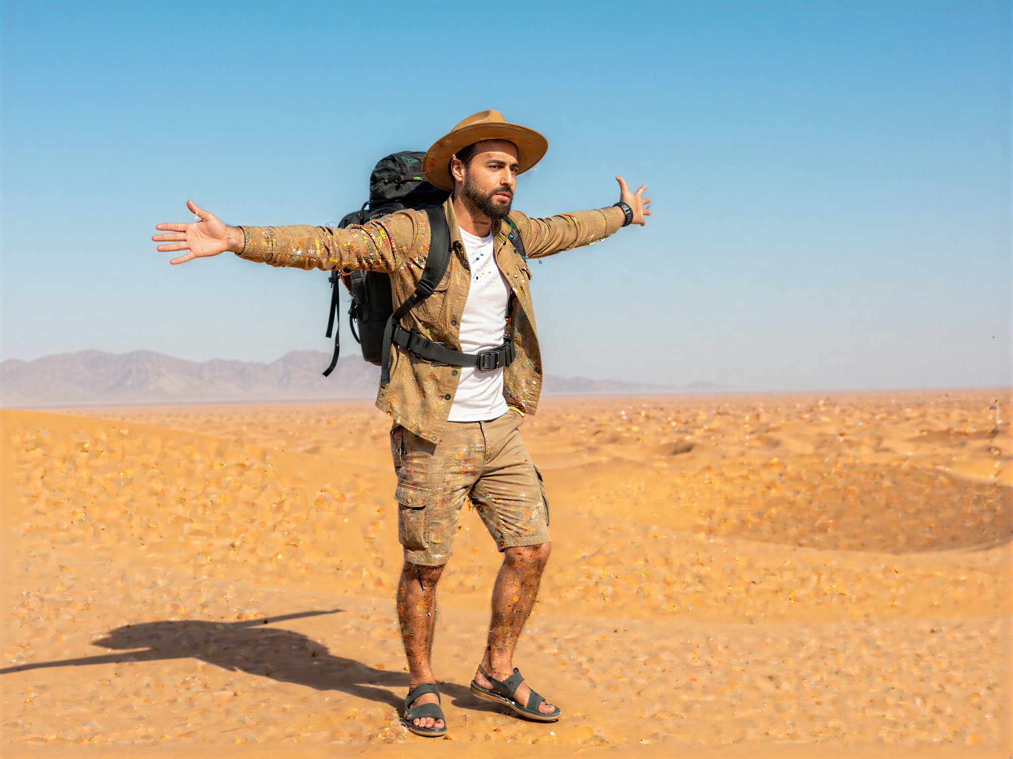 A 32-year-old male adventurer, OD62S, captured in a moment of joy amidst a stunning desert landscape. He wears a lightweight, khaki utility shirt and cargo shorts, complemented by rugged sandals and a wide-brimmed hat. His tanned skin glows under the brilliant sun, and he carries a lightweight backpack filled with gear for exploration. The background features rolling sand dunes under a vast blue sky, creating a sense of freedom and adventure. His laughter is frozen in time, reflecting a carefree spirit, as he stands atop a dune, arms outstretched, embracing the warm desert breeze. The composition is infused with vibrant colors and dynamic lighting that emphasizes the richness of the surroundings, evoking a mood of happiness and adventure.