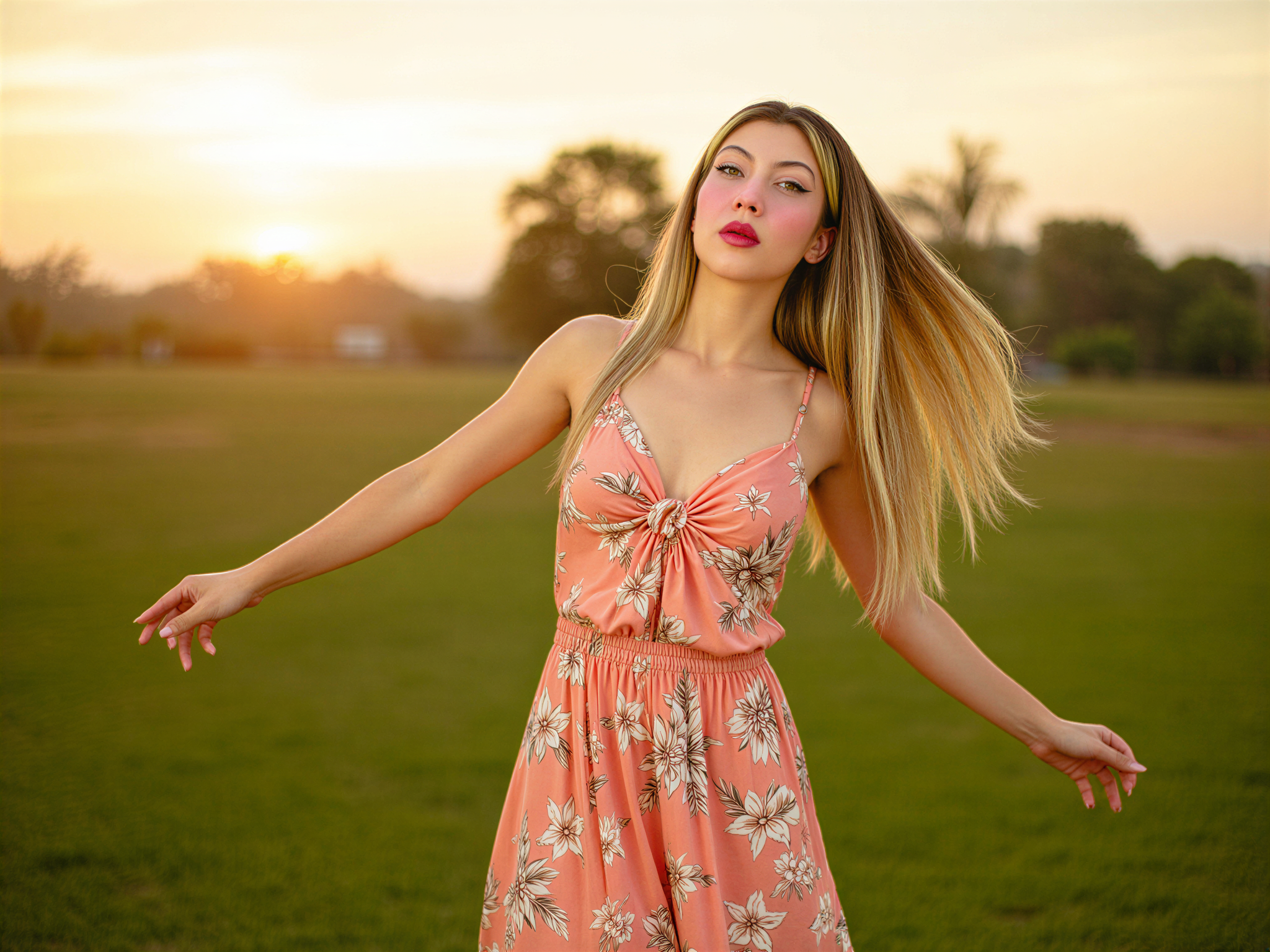 A joyful female individual, OD62S, aged 28, exuding an infectious happiness against the vibrant backdrop of a lush Thai landscape. She sports a flowing, floral-print maxi dress in bright tropical hues that dance around her as she twirls. Her sun-kissed skin glows under the warm light, and her hair cascades in soft waves, adorned with fresh jasmine flowers. The composition captures her mid-laugh, arms open wide as if embracing the beauty of nature around her. The setting sun casts a golden glow, enhancing the idyllic scene, evoking a sense of freedom and joy that reflects the spirit of Thailand. The image combines a sense of playfulness with cultural richness, positioned within a dreamy, travel-inspired editorial frame.