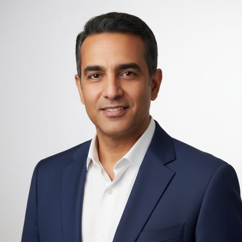 Professional headshot of a man with dark hair, wearing a navy suit and white shirt, smiling against a plain white background.