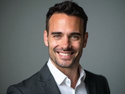 Smiling man in a suit against a gray background, representing professionalism and confidence.