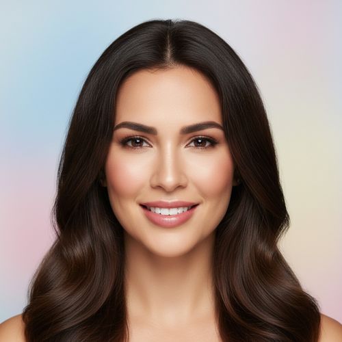 Close-up portrait of a smiling woman with long, wavy dark hair and natural makeup against a soft pastel background.