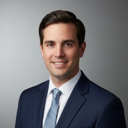 Professional headshot of a man wearing a navy suit and patterned tie, smiling against a light gray background.