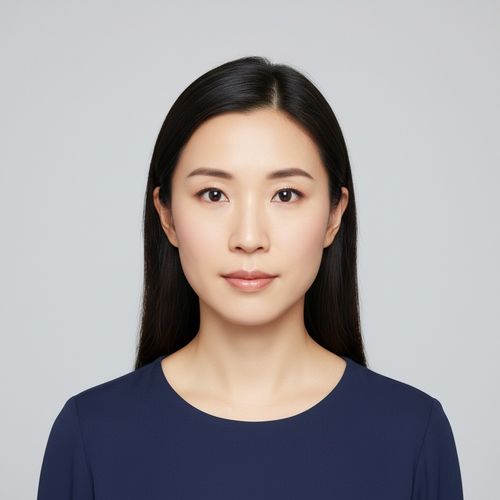 Headshot of a woman with straight, dark hair wearing a navy blue shirt, looking directly at the camera against a light gray background.