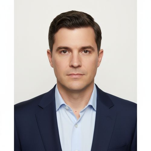 Professional headshot of a man in a navy blazer and light blue shirt, with short hair and a neutral expression against a plain white background.