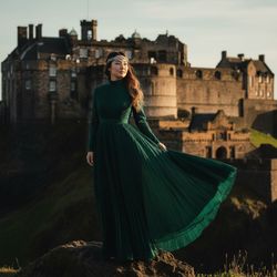 Jane, a 23-year-old Asian woman, stands majestically in front of the iconic Edinburgh Castle. She embodies the spirit of a historical figure with a modern twist, dressed in a flowing deep emerald chiffon georgette gown that catches the cool Scottish winds. The dress features delicate hand-pleats and a high collar, highlighting her elegant neck. Styled in loose waves and adorned with a silver circlet reminiscent of Celtic motifs, her luminous complexion is accentuated by late afternoon light. She stands poised on a slight rise, her silhouette contrasting with the castle's battlements, telling a story of resilience and nobility amidst Scotland's rich history, evoking themes worthy of a fashion editorial.  The composition is designed with the rule of thirds, emphasizing her regal presence and the grandeur of the setting.